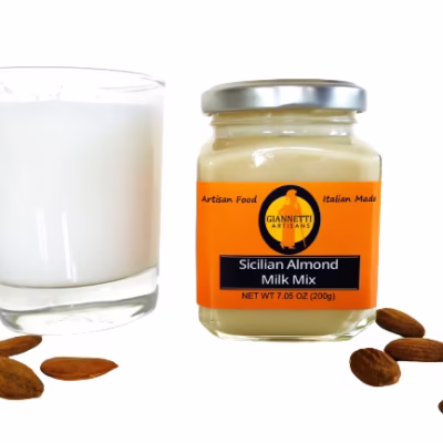 A jar of Giannetti Artisans Sicilian Almond Paste with a glass containing the actual almond milk with almonds around the glass and jar on a white background