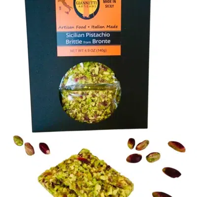 Front view of a black package of Giannetti Artisans Sicilian Pistachio Brittle with a piece of brittle and loose pistachios in front.